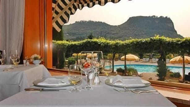 A dining table set for two with a view of a pool and mountains. - Hotel Garden (Garda)