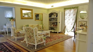 A living room with a floral sofa, a white coffee table, a bookshelf, and a patterned rug. - Hotel Garden (Garda)