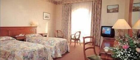 Een hotelkamer met twee bedden, een bureau met een televisie, een stoel en een raam met gordijnen.