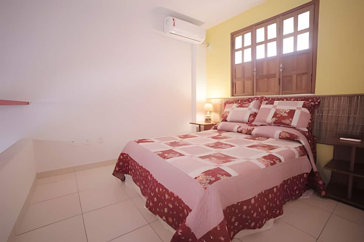 Une chambre à coucher avec un lit, une table de chevet, une lampe et une fenêtre avec des stores.