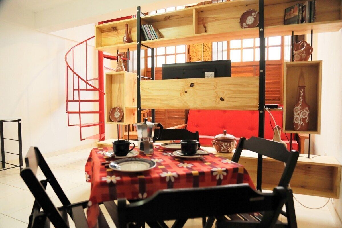 A dining area with a table set for two, surrounded by black chairs. A red spiral staircase leads to a lofted seating area above.