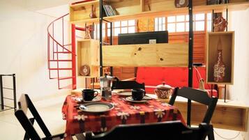 A dining area with a table set for two, surrounded by black chairs. A red spiral staircase leads to a lofted seating area above.
