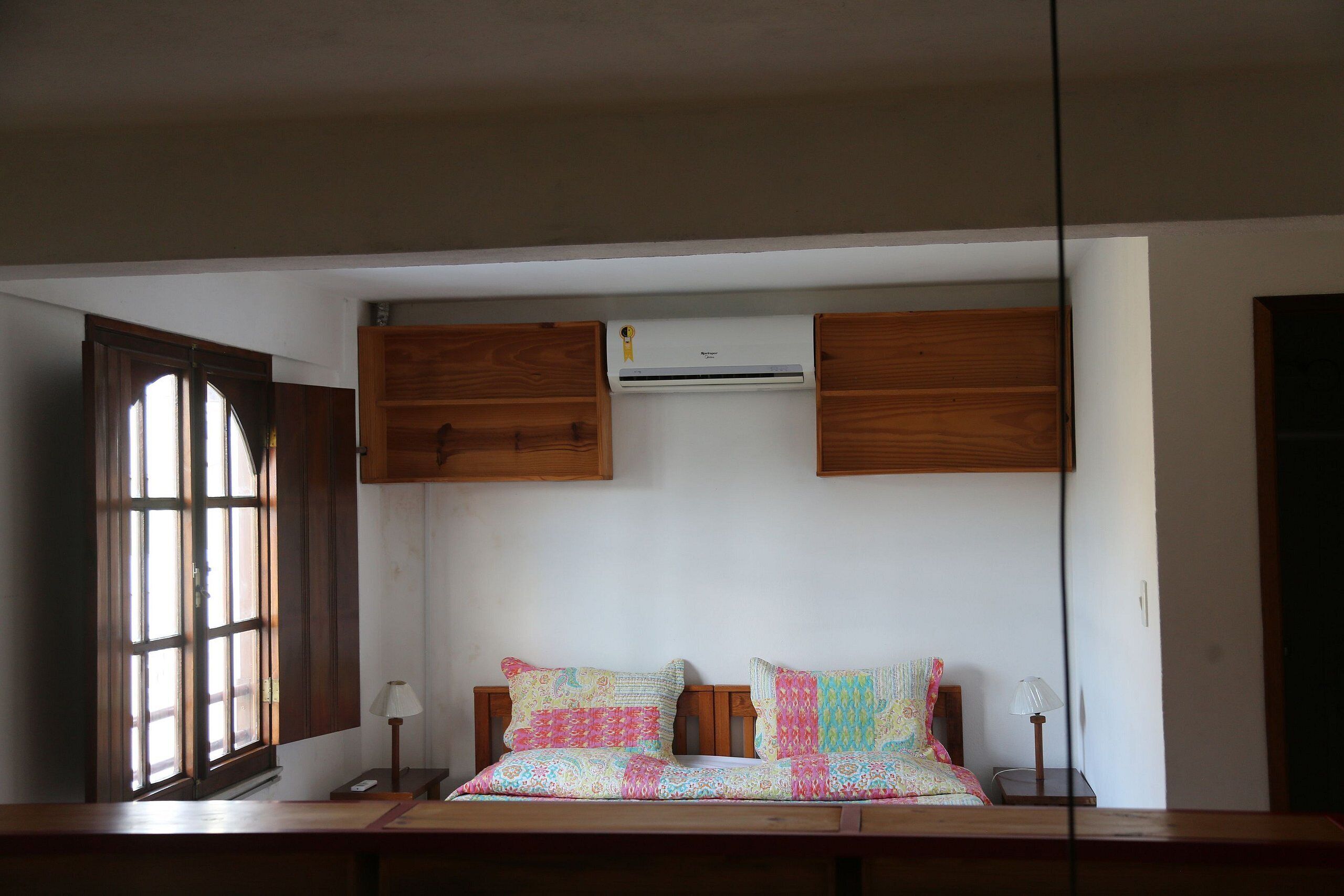 A bedroom with a bed, wooden headboard, bedside tables, and an air conditioning unit mounted on the wall.
