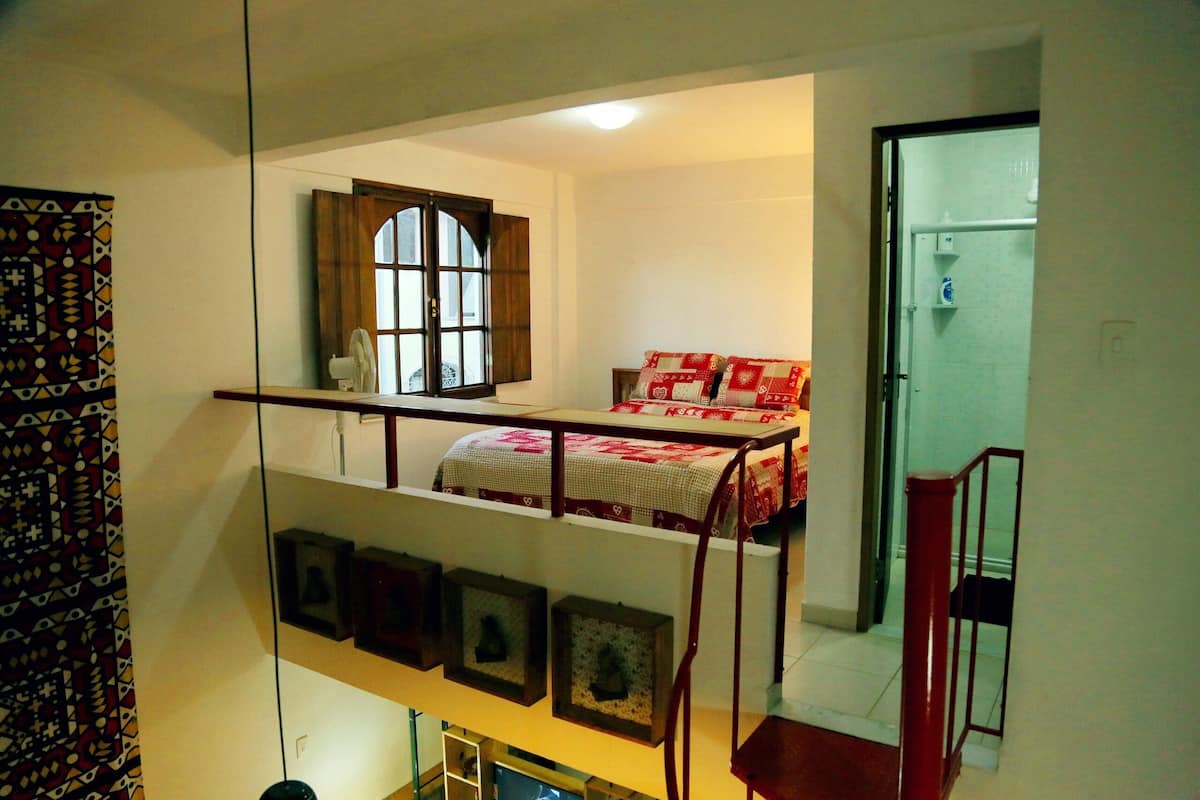 Une chambre avec un lit superposé, une fenêtre avec des volets en bois et une porte donnant sur une salle de bain.