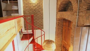 Un escalier avec des rampes rouges menant à un niveau inférieur, une lampe en osier et un mur de briques agrémenté d’un luminaire.