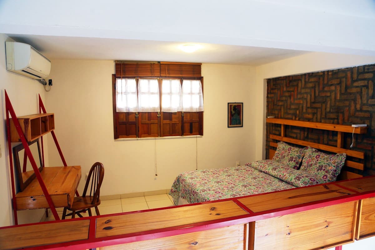 Une chambre à coucher avec un lit en bois, un bureau, une chaise et une fenêtre avec des rideaux.