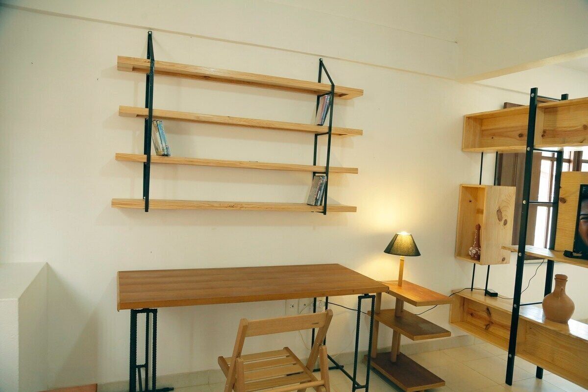 A room with a wooden desk, a chair, and a wall-mounted shelf with books.