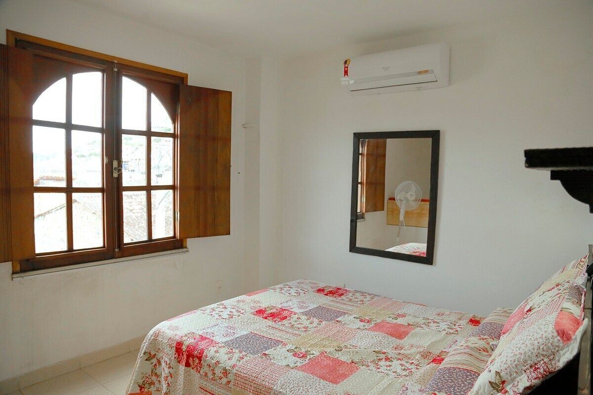 A bedroom with a bed, a window with wooden shutters, a wall-mounted air conditioner, and a mirror.