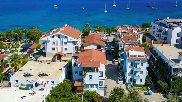 Zona residencial costera con edificios, mar azul cristalino y barcos.