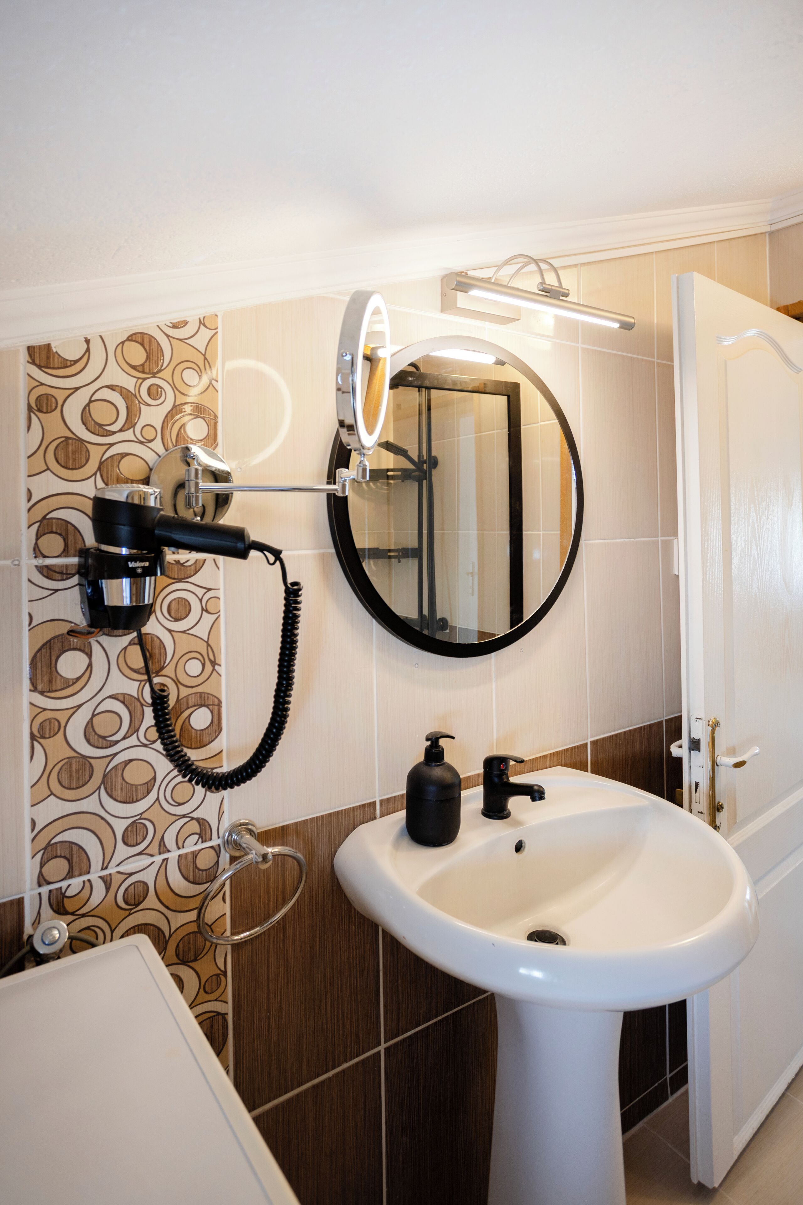 A bathroom with a white sink, a mirror, and a hairdryer mounted on the wall.