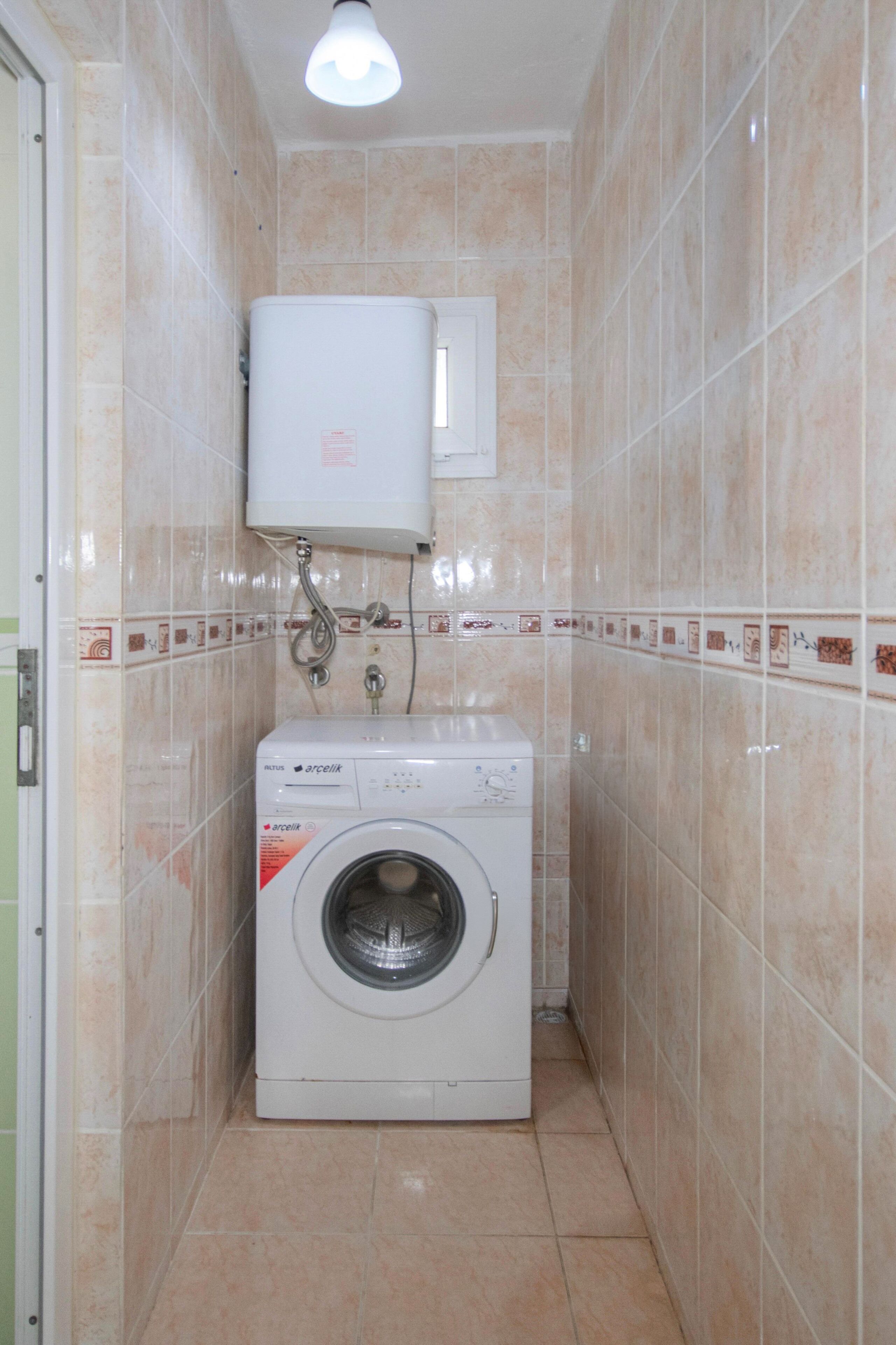 A compact laundry room with a washing machine, a water heater, and tiled walls.