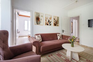 Un salón con un sofá marrón, una mesa de centro redonda y tres obras de arte abstracto en la pared.