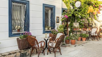 Uma área externa com mesas e cadeiras de vime, plantas em vasos e um aviso indicando Wi-Fi gratuito.