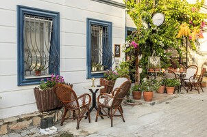 Un área de estar al aire libre con sillas y mesas de mimbre, plantas en macetas y un cartel que indica Wi-Fi gratuito.