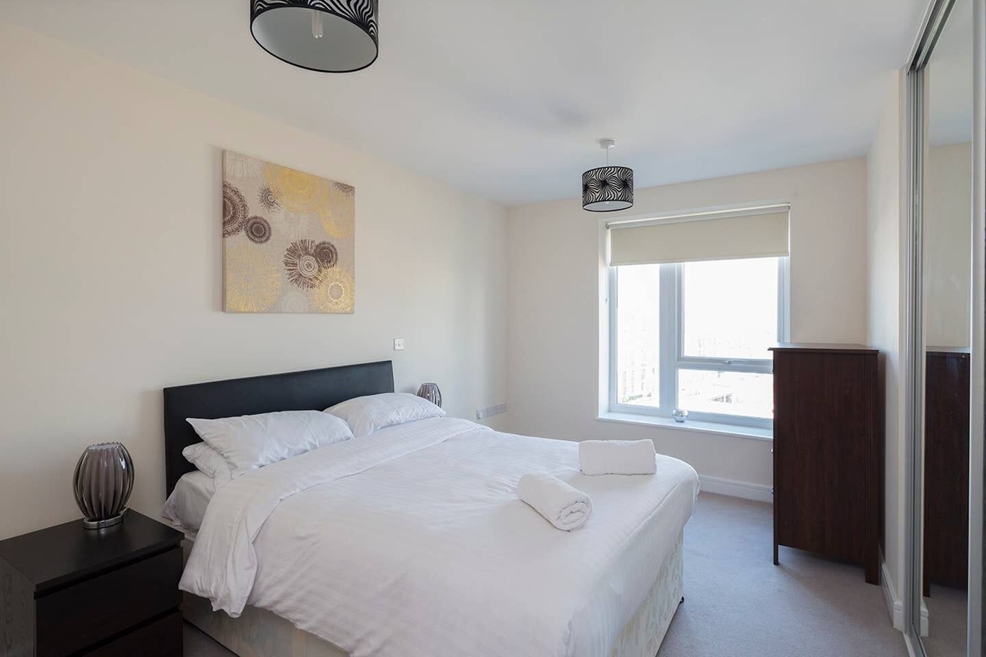 A bedroom with a bed, bedside tables, a window, and a painting on the wall.