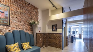 A modern lobby with a brick wall, a blue sofa with patterned cushions, and a Heineken beer poster.