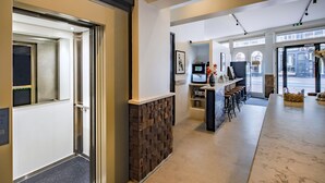 A modern hotel lobby with a marble reception desk, a stone accent wall, and a bar area with stools.