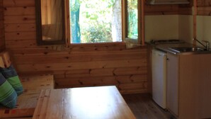 A wooden cabin interior with a wooden table, a bench, a window, and a kitchenette. - Pirineos Cien Lagos (Esterri D'Aneu)
