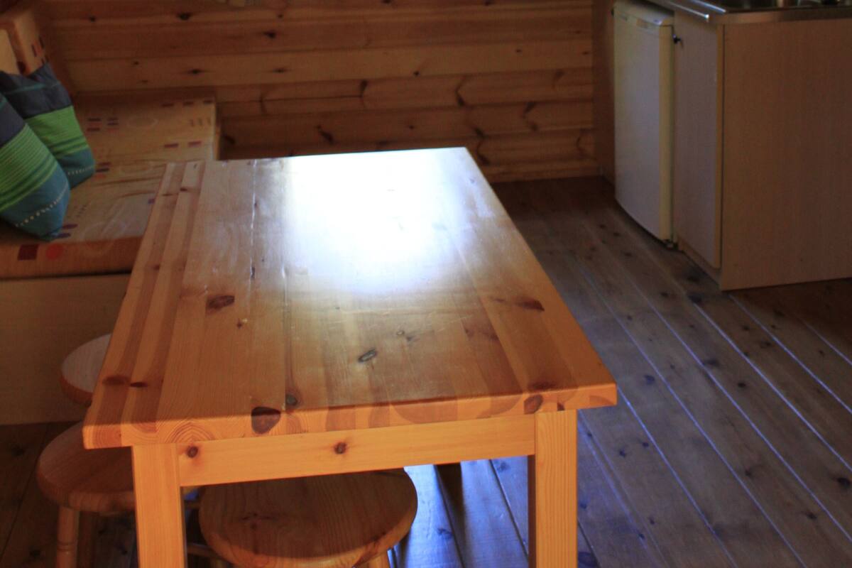 L’intérieur d’une cabane en bois, avec une table en bois, un banc, une fenêtre et un coin cuisine.
