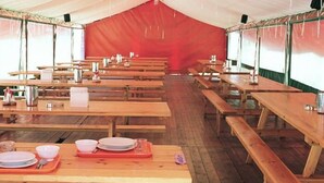A large tent with multiple wooden tables and benches, arranged in rows. - Pirineos Cien Lagos (Esterri D'Aneu)