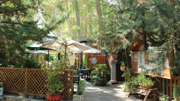 An outdoor patio area with wooden tables and chairs, surrounded by potted plants and a wooden fence. - Pirineos Cien Lagos (Esterri D'Aneu)