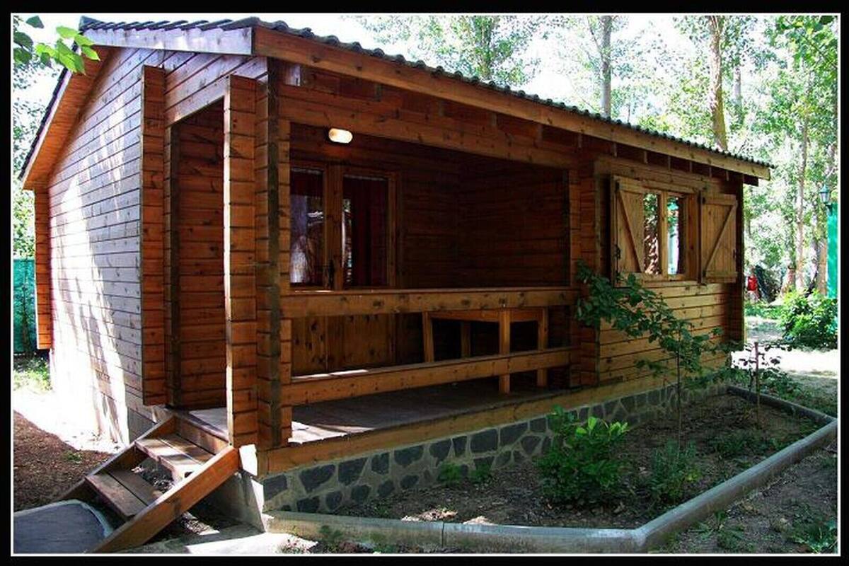 Une cabane en bois avec un porche, des fondations en pierre et un petit jardin.