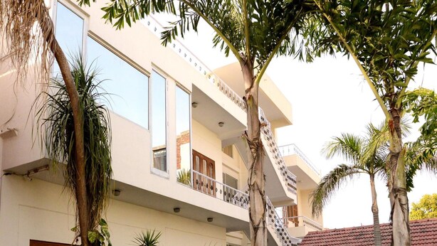 Un immeuble à plusieurs étages doté de balcons, entouré d’une végétation luxuriante et de palmiers.