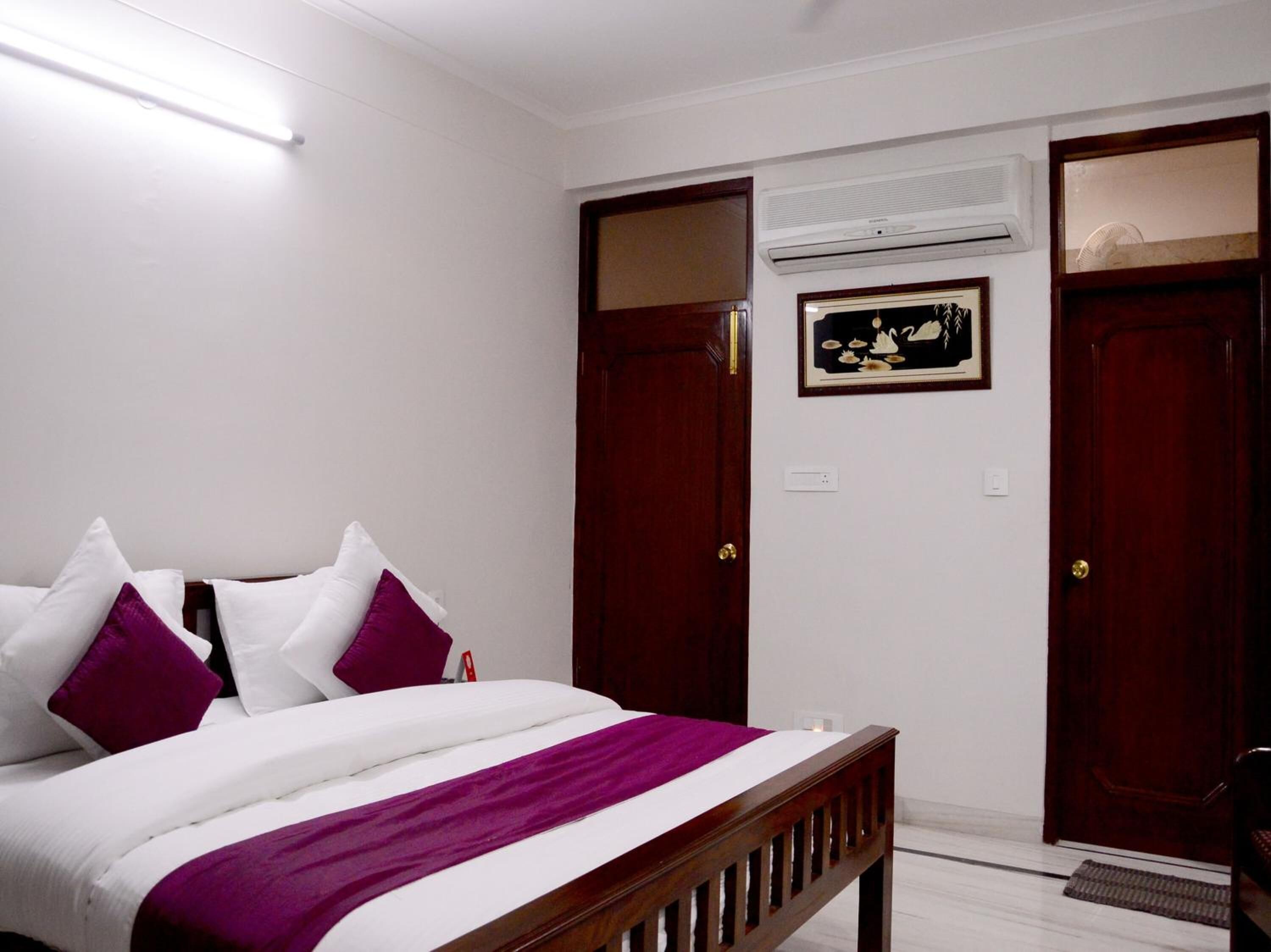 Un dormitorio con una cama, dos puertas, un equipo de aire acondicionado y un cuadro en la pared.