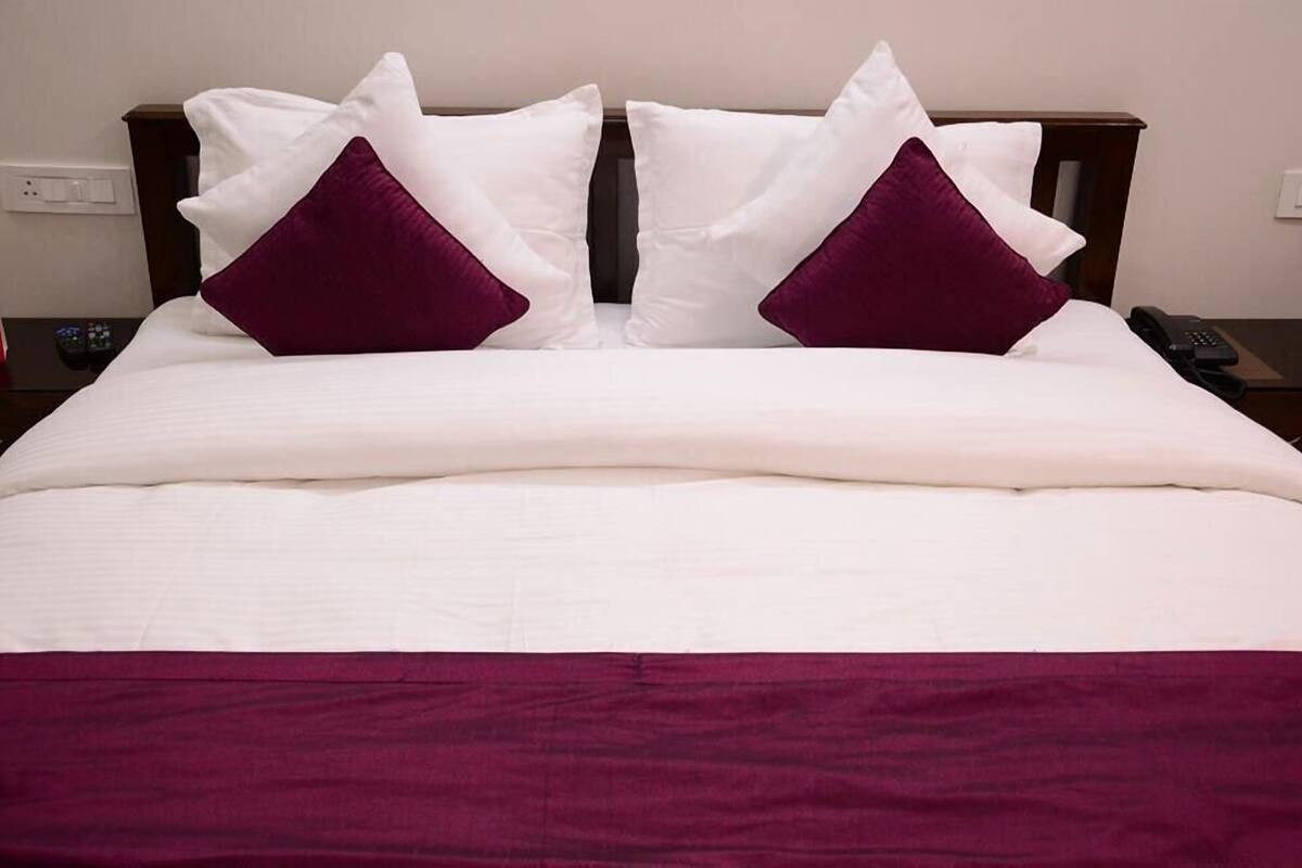 Ein ordentlich bezogenes Bett mit weißer und violetter Bettwäsche, ein hölzerner Kopfteil und ein Nachttisch mit einem Telefon.
