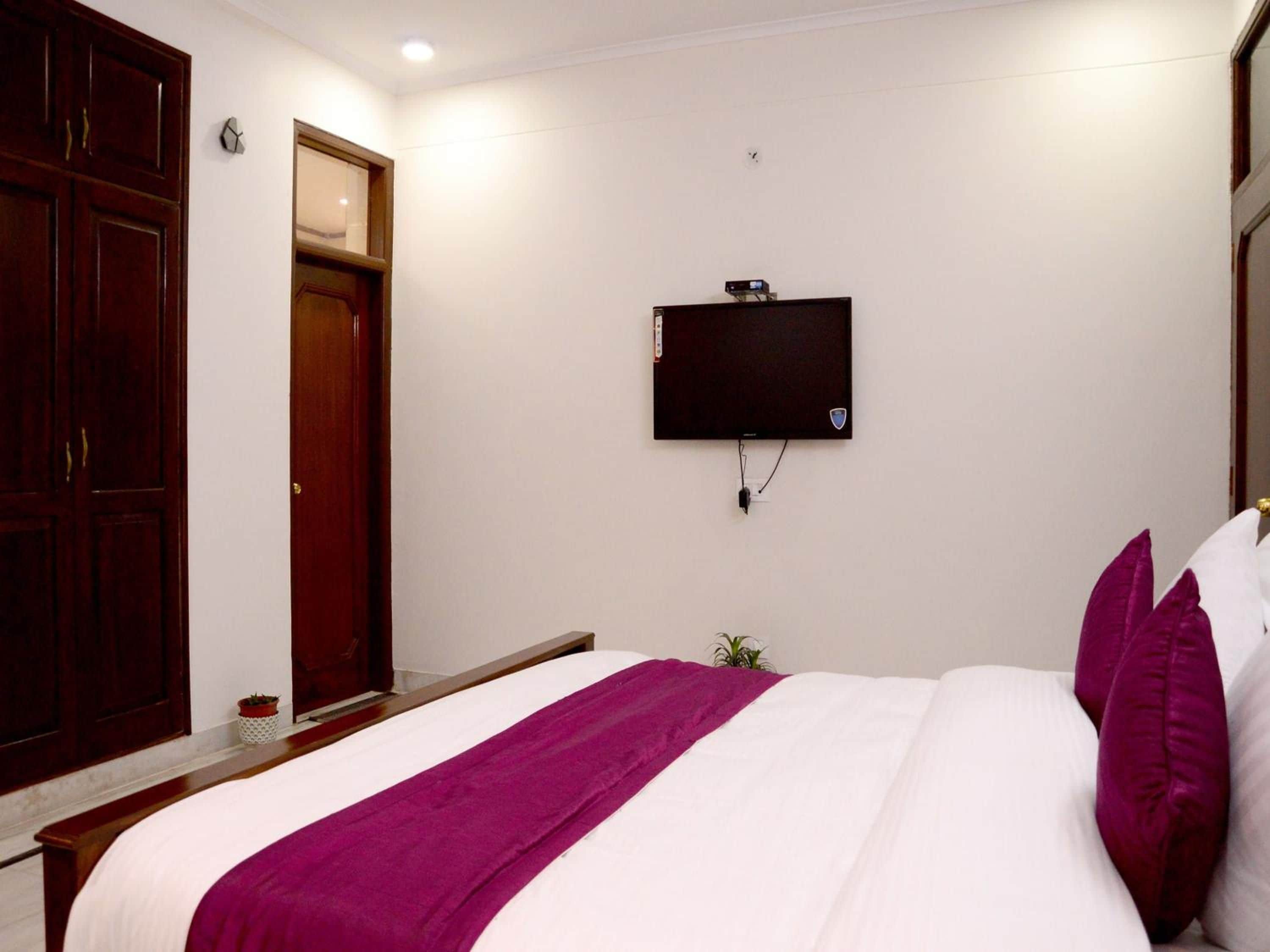 A bedroom with a bed, a television mounted on the wall, and a wooden wardrobe.