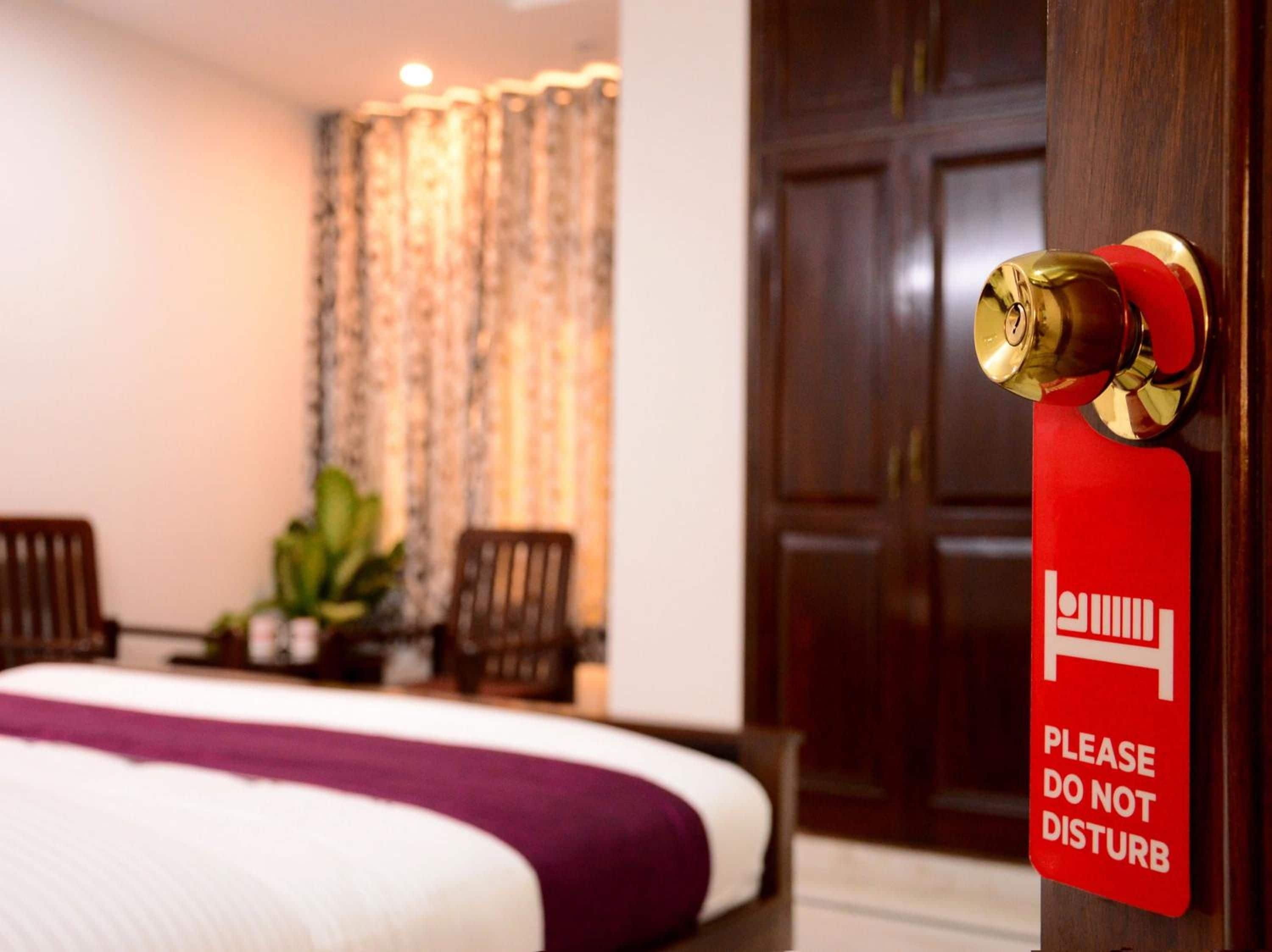 Una habitación de hotel con una cama, un letrero rojo de 'No molestar' y una puerta de madera.