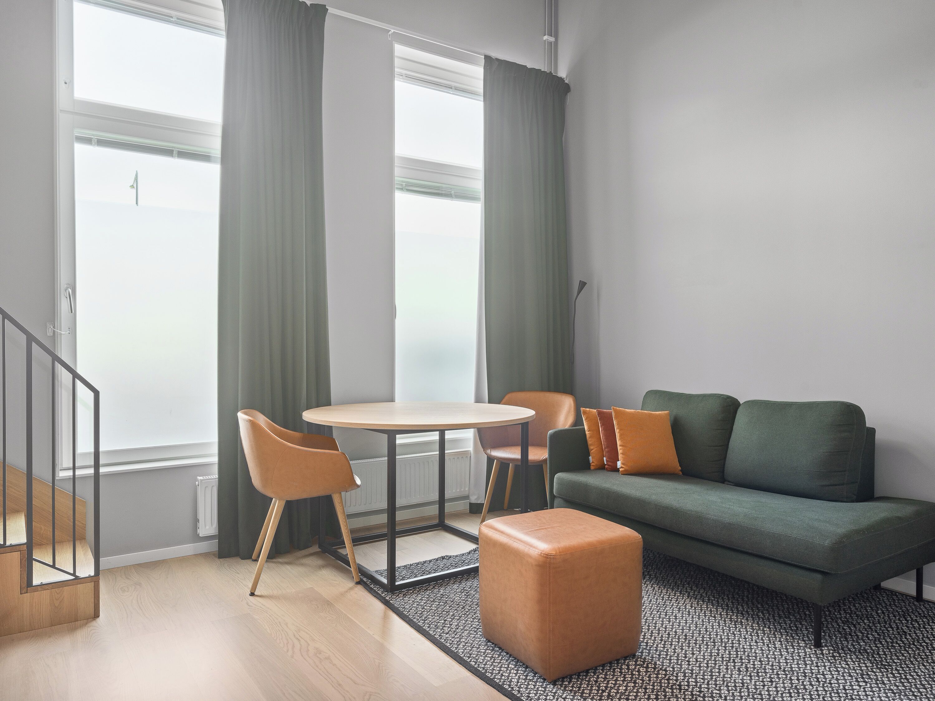 A modern living room with a round table, two chairs, a sofa, and a small ottoman.