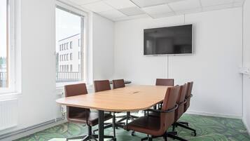 A conference room with a large table, six chairs, a flat-screen TV, and a window with a view of buildings.