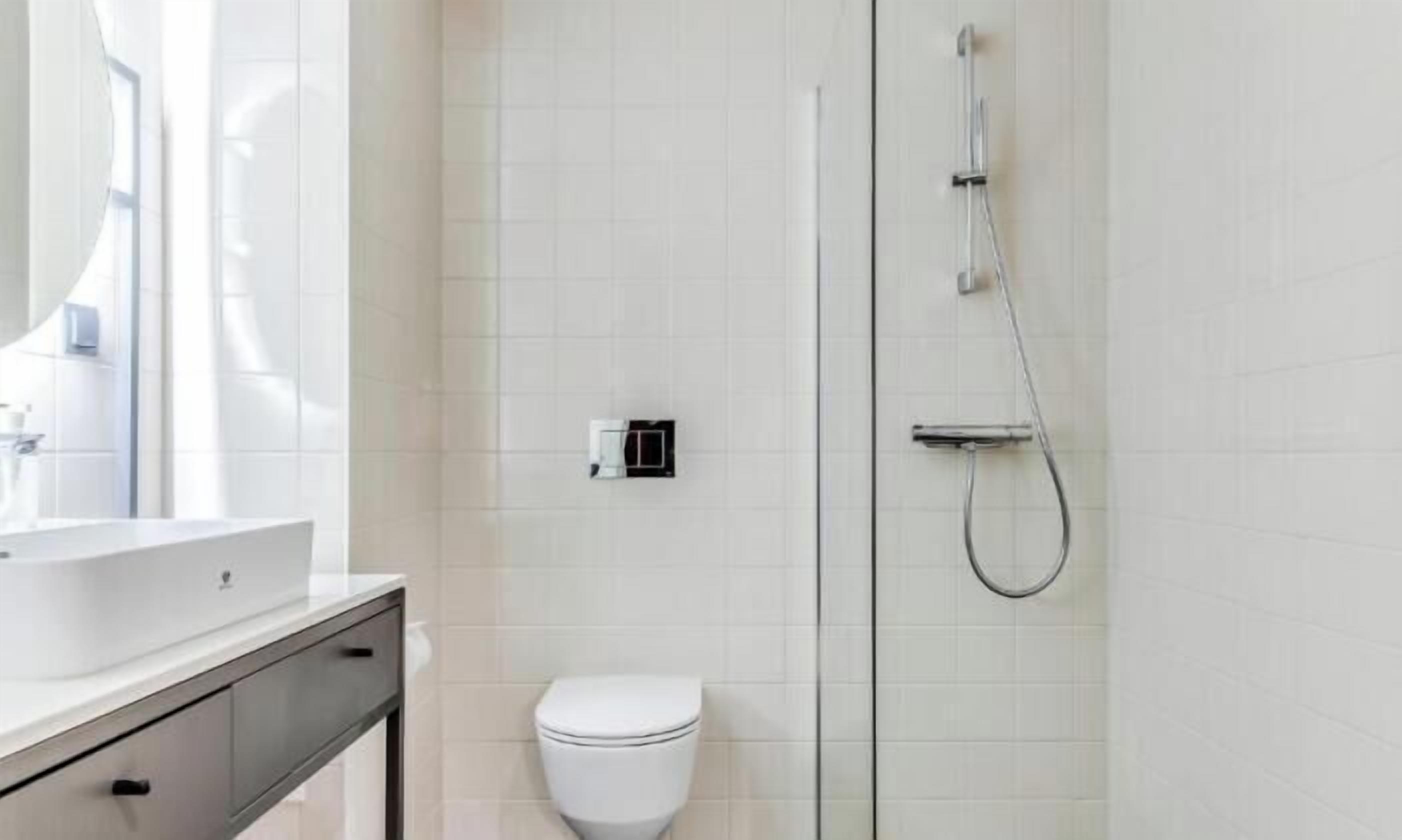 Ein modernes Badezimmer mit Toilette in Weiß, einer Duschkabine aus Glas und einem Waschbecken mit Spiegel.