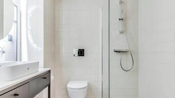 Ein modernes Badezimmer mit Toilette in Weiß, einer Duschkabine aus Glas und einem Waschbecken mit Spiegel.