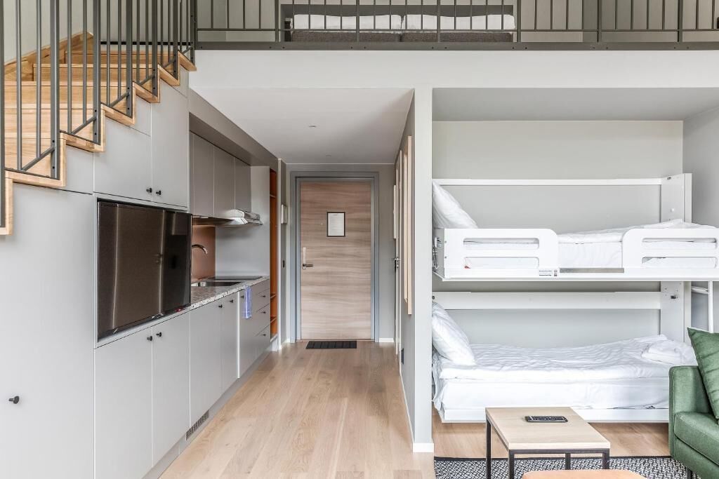 A compact, modern apartment with a kitchenette, a loft bedroom with a bunk bed, and a staircase leading to an upper level.