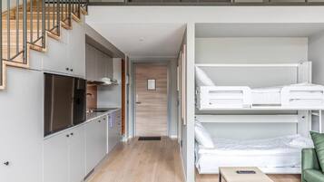 A compact, modern apartment with a kitchenette, a loft bedroom with a bunk bed, and a staircase leading to an upper level.
