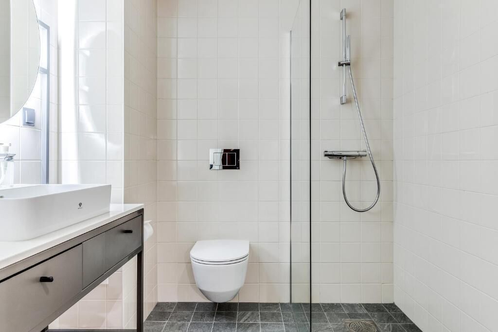 A modern bathroom with a white toilet, a glass shower enclosure, and a white sink with a mirror.