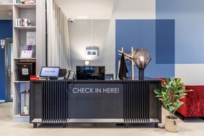 A reception desk with a "CHECK IN HERE!" sign, a computer, a telephone, and a potted plant. - Part-Time Home Täby (Taby)