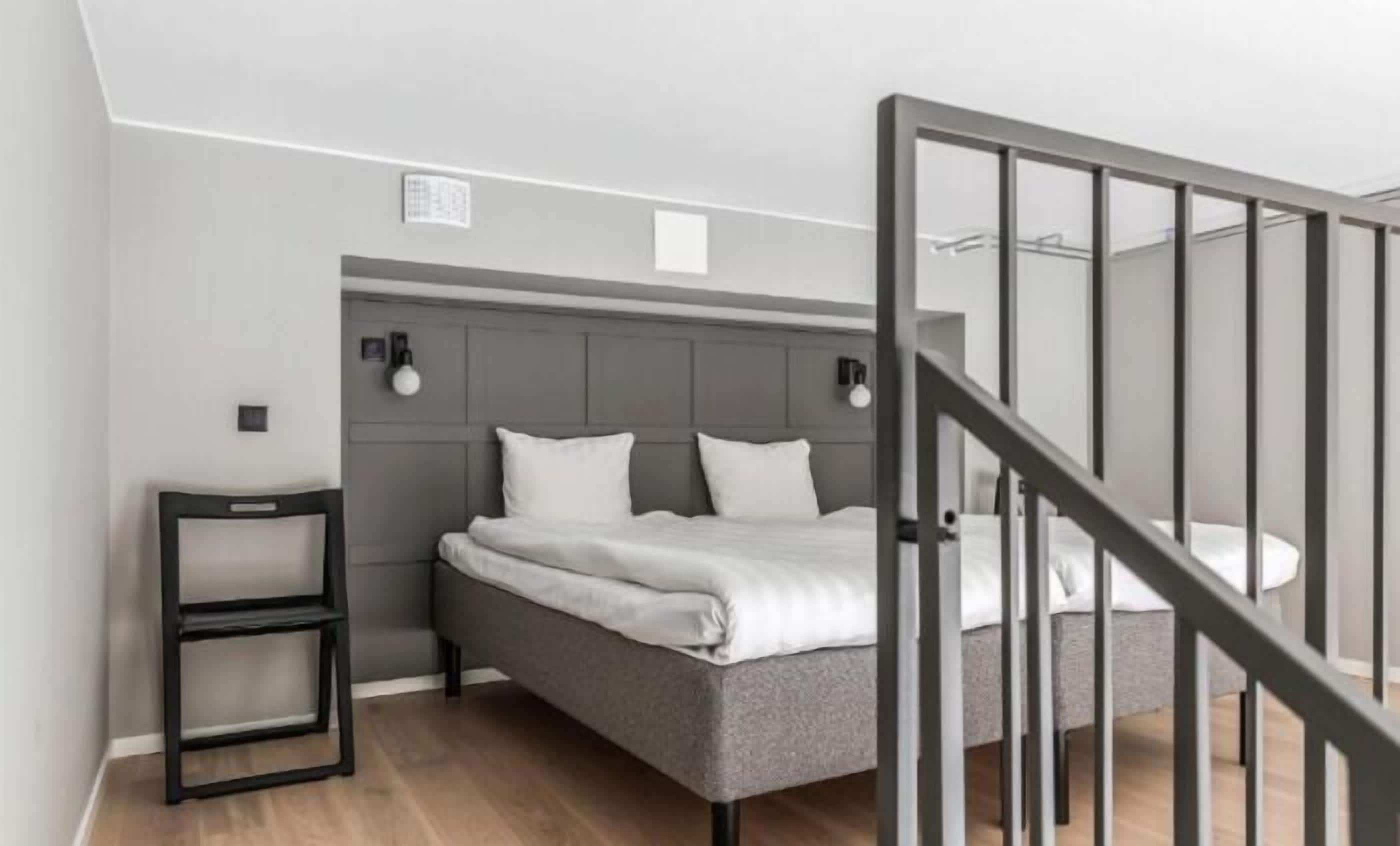Un dormitorio moderno con una cama tapizada de gris, una mesita de noche pequeña y una escalera con barandilla negra.