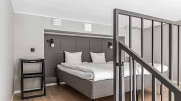 Un dormitorio moderno con una cama tapizada de gris, una mesita de noche pequeña y una escalera con barandilla negra.