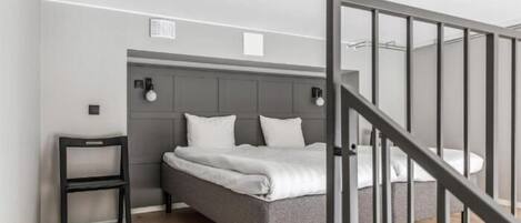 Un dormitorio moderno con una cama tapizada de gris, una mesita de noche pequeña y una escalera con barandilla negra.