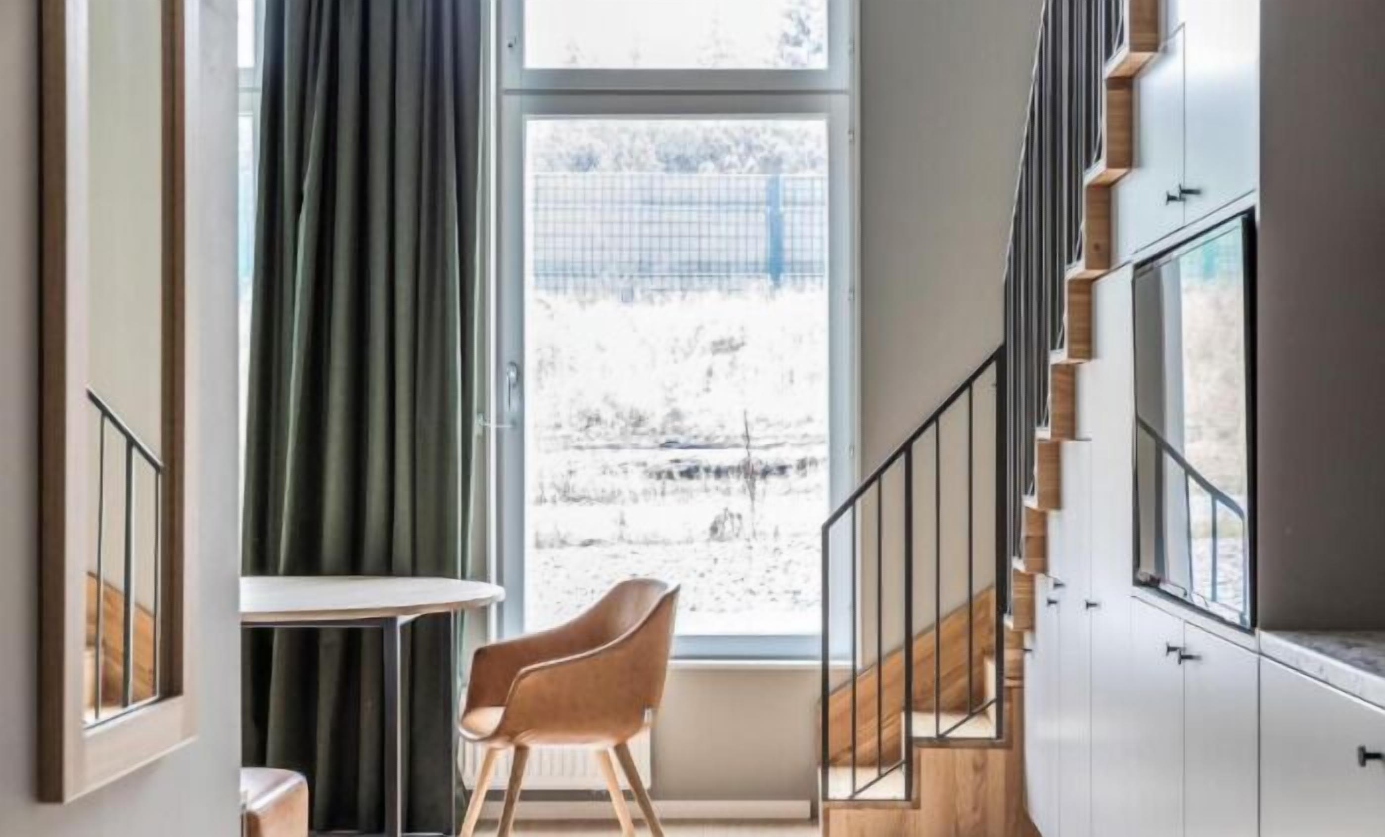 Un intérieur moderne avec un escalier, une fenêtre avec des rideaux et une chaise en bois.