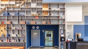 A modern reception area with a check-in counter, a seating area with a sofa and a table, and a large bookshelf filled with books. - Part-Time Home Täby (Taby)