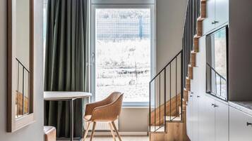 A modern interior with a staircase, a view through a window, and a chair by the window.