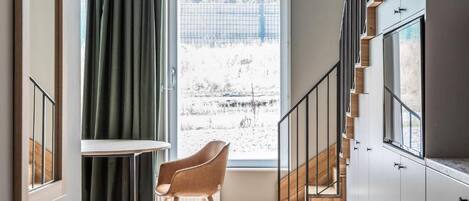 A modern interior with a staircase, a view through a window, and a chair by the window.