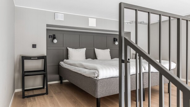 A modern bedroom with a grey bed, two bedside tables with lamps, and a staircase. - Part-Time Home Täby (Taby)
