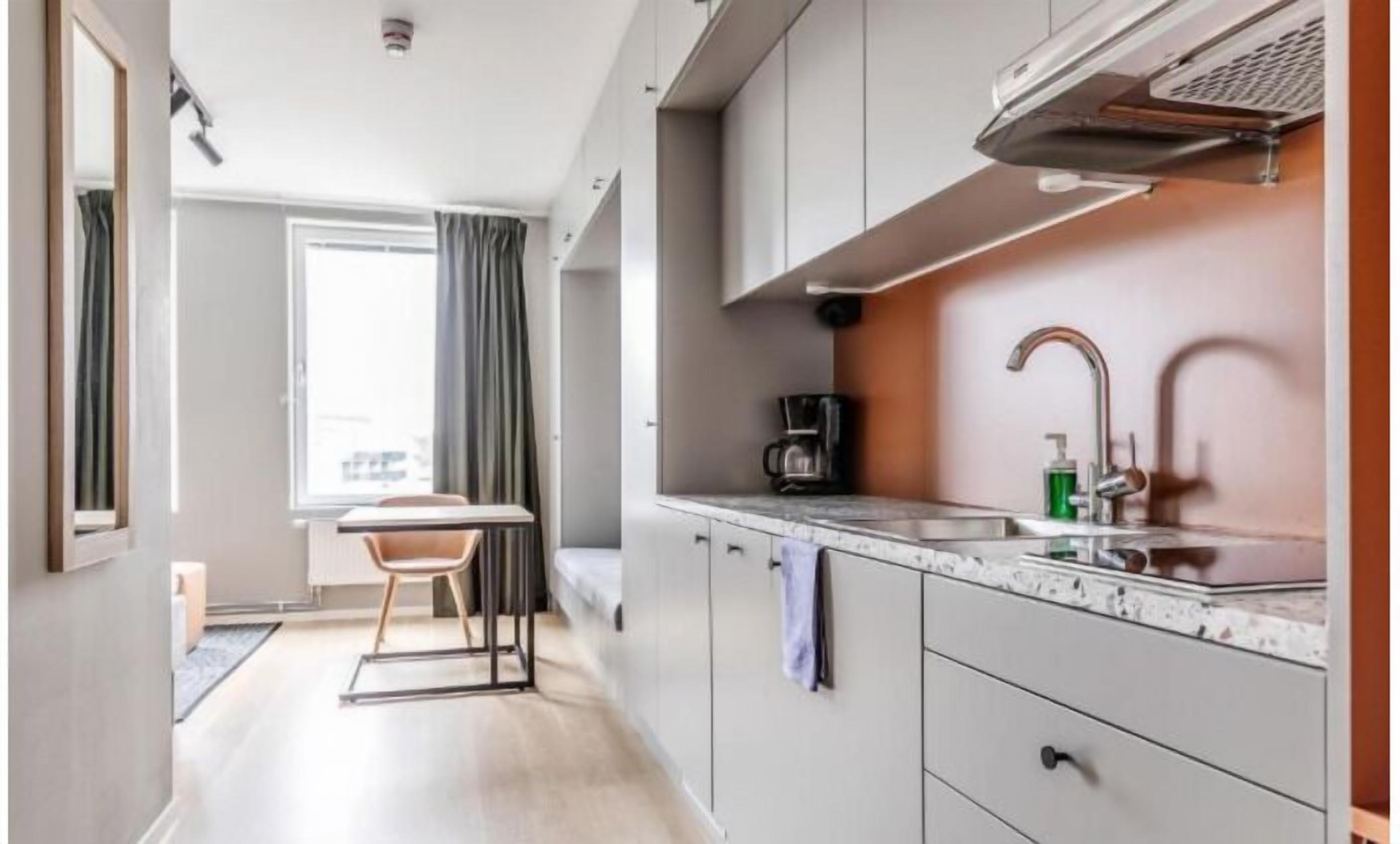 Cocina compacta con cafetera, lavamanos y armarios.