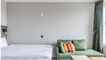 Ett hotellrum med en säng, en grön soffa med kuddar, ett litet bord och ett fönster med gardiner.