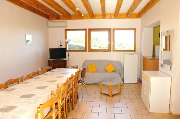 A room with a dining table, chairs, a sofa, a television, and a refrigerator.